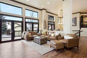 Living room featuring a high ceiling, crown molding, hardwood / wood-style flooring, and suspended lighting