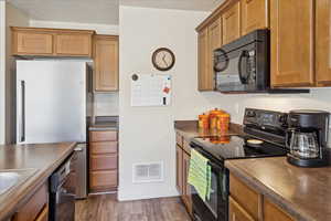 Kitchen featuring black appliances, dark wood finished floors, dark countertops, and wood finish cabinetry
