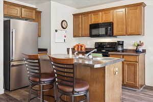 Kitchen featuring black appliances, wood finish cabinets, dark countertops, and dark wood-style floors