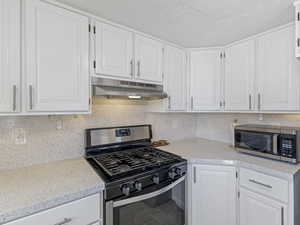 Kitchen with stainless steel appliances, white cabinetry, decorative backsplash, and a textured ceiling