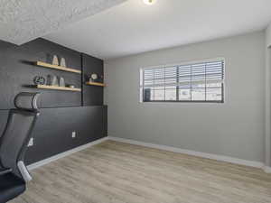 Unfurnished office featuring light wood-type flooring, a textured ceiling, and a textured wall