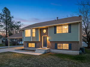Bi-level home with a chimney, a front lawn, brick siding, and roof with shingles