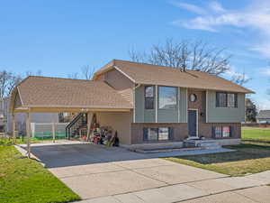 Bi-level home with an attached carport, driveway, roof with shingles, and brick siding
