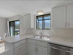 Kitchen featuring white cabinets, dishwasher, tasteful backsplash, a peninsula, and a textured ceiling