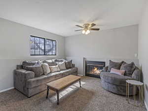 Living room featuring a fireplace with flush hearth, carpet, and a ceiling fan