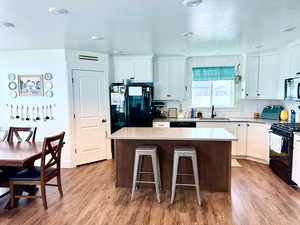 Kitchen with white cabinets, a center island, black appliances, light wood finished floors, and a kitchen bar