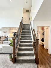 Stairs with a high ceiling, wood finished floors, and recessed lighting