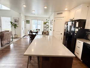 Kitchen featuring white cabinetry, dark wood finished floors, black appliances, a kitchen island, and a breakfast bar