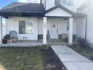 Entrance to property featuring a large porch, a shingled roof, and a lawn