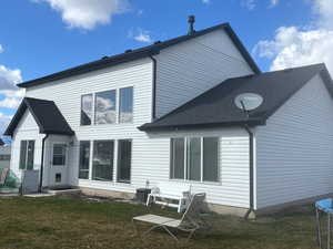 Rear view of house featuring a yard, a shingled roof, and a trampoline