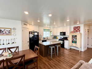 Two tone kitchen with a center island, black appliances, dark wood finished floors, a kitchen bar, and dual tone cabinetry