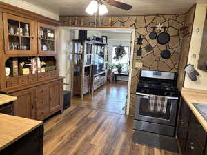 Kitchen featuring light countertops, stainless steel range with gas stovetop, a ceiling fan, glass insert cabinets, and dark wood finished floors
