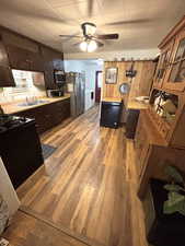 Kitchen with a ceiling fan, wood finished floors, black appliances, dark wood finish cabinets, and light countertops