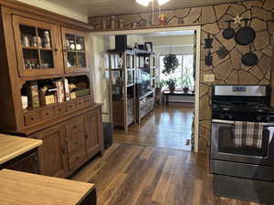 Kitchen featuring stainless steel range with gas cooktop, wood finish cabinetry, dark wood-type flooring, and glass insert cabinets