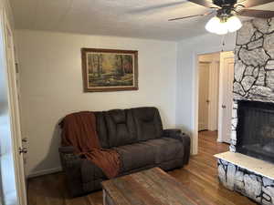 Living area with a stone fireplace, dark wood finished floors, and ceiling fan