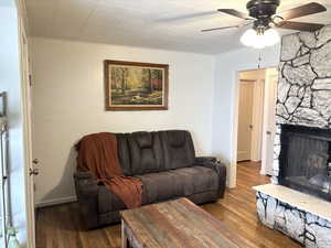 Living area with a stone fireplace, dark wood-type flooring, and ceiling fan