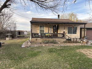 View of front of property with covered porch, a chimney, a front lawn, and a shingled roof