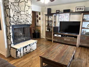 Living area featuring a stone fireplace, ceiling fan, and wood finished floors