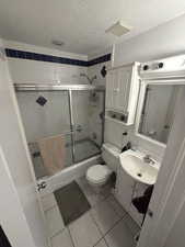 Bathroom with vanity, a textured ceiling, light tile patterned floors, and enclosed tub / shower combo