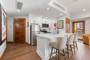 Kitchen with white cabinetry, a kitchen breakfast bar, dark wood-style flooring, stainless steel appliances, and an island with sink