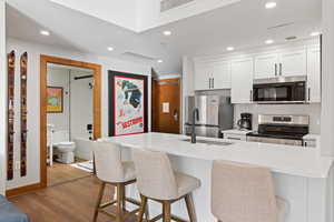 Kitchen with white cabinetry, stainless steel appliances, recessed lighting, a kitchen breakfast bar, and dark wood finished floors