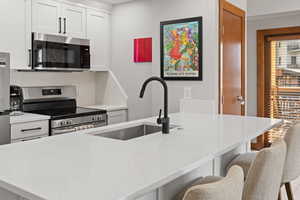 Kitchen featuring stainless steel appliances, white cabinetry, light stone counters, and a kitchen island with sink