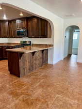 Kitchen with dark wood finish cabinets, arched walkways, a peninsula, a breakfast bar, and stainless steel appliances