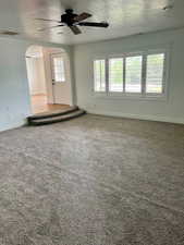 Unfurnished living room with arched walkways, ceiling fan, carpet floors, and a textured ceiling