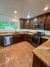 Kitchen with dark wood finish cabinetry, stainless steel appliances, light stone countertops, recessed lighting, and light tile patterned floors