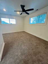 Spare room featuring dark colored carpet, plenty of natural light, and a ceiling fan