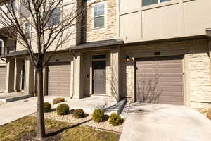 View of exterior entry featuring a garage, concrete driveway, brick siding, and stone siding
