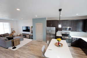 Kitchen featuring stainless steel appliances, open floor plan, light wood-type flooring, dark wood finish cabinets, and tasteful backsplash