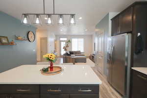 Kitchen with dark wood finish cabinets, open floor plan, stainless steel fridge, a center island, and decorative light fixtures
