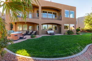 Back of property with a hot tub, outdoor furniture, stucco siding, and a balcony