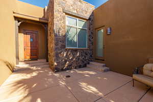 Property entrance with stone siding, stucco siding, and a patio