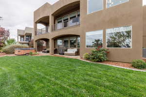 Rear view of house with a hot tub, stucco siding, a balcony, a patio, and outdoor lounge area