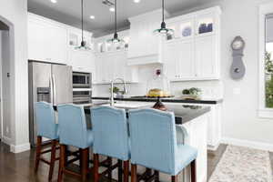Kitchen with lighted glass fronted cabinets, stainless steel appliances, a kitchen breakfast bar, and white cabinetry