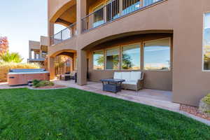 Rear view of house with outdoor lounge area, stucco siding, a hot tub, a patio, and a lawn