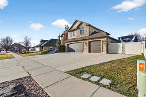 View of front of house with a gate, stone siding, driveway, a residential view, and an attached garage