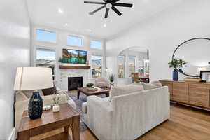 Living area featuring a high ceiling, a tile fireplace, arched walkways, a ceiling fan, and wood finished floors