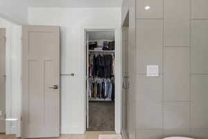 Full bathroom with a spacious closet, a shower stall, and light tile patterned flooring
