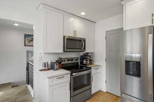 Kitchen with stainless steel appliances, white cabinets, backsplash, and recessed lighting