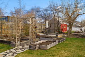 Fenced backyard featuring a vegetable garden, an outdoor structure, and a patio area