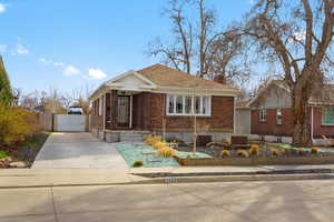 Bungalow-style house with brick siding, a chimney, roof with shingles, and driveway
