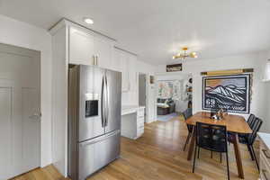 Kitchen featuring stainless steel refrigerator with ice dispenser, white cabinets, a chandelier, and light wood finished floors