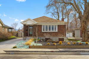 View of front facade featuring a chimney, brick siding, and a shingled roof