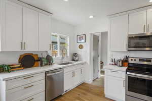Kitchen with stainless steel appliances, white cabinets, decorative backsplash, light wood-style floors, and recessed lighting