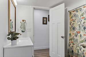 Bathroom with a textured ceiling, a shower with curtain, dark wood-style floors, and vanity