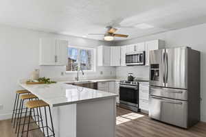 Kitchen with stainless steel appliances, a peninsula, a kitchen bar, a ceiling fan, and light stone counters