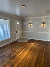 Entrance foyer with dark wood-style flooring, a textured ceiling, and crown molding